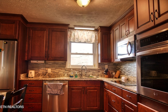 kitchen featuring light stone countertops, appliances with stainless steel finishes, backsplash, a textured ceiling, and sink