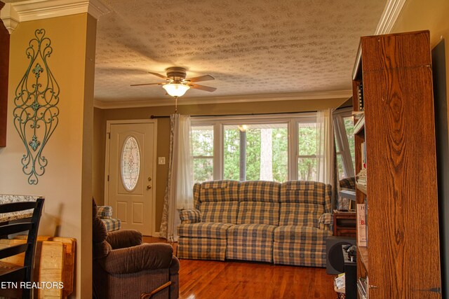 living room with ceiling fan, wood-type flooring, a textured ceiling, and ornamental molding