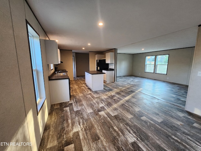 kitchen with white cabinetry, black fridge, a center island, and dark wood-type flooring