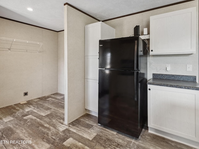 kitchen featuring dark wood-type flooring, white cabinets, crown molding, and black fridge