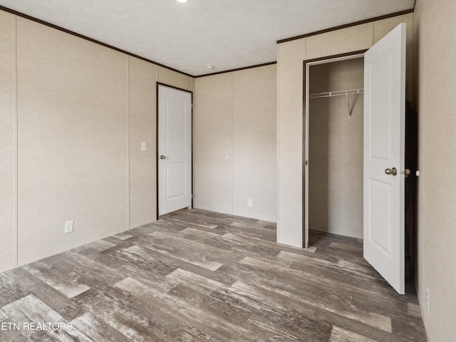 unfurnished bedroom with hardwood / wood-style flooring, crown molding, a textured ceiling, and a closet