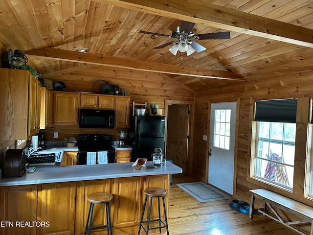 kitchen with black appliances, vaulted ceiling with beams, kitchen peninsula, and wooden walls