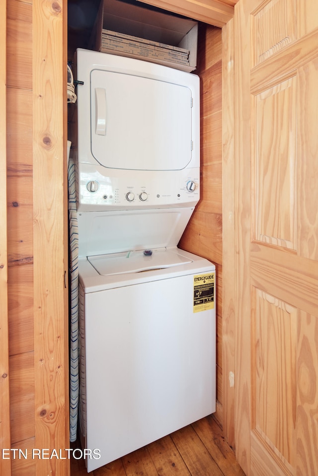 laundry room with wood walls, stacked washing maching and dryer, and wood-type flooring