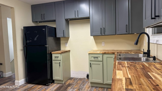 kitchen with wood counters, black fridge, sink, green cabinetry, and dark hardwood / wood-style floors