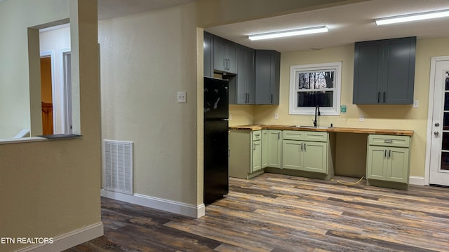 kitchen featuring sink, dark hardwood / wood-style flooring, wooden counters, black refrigerator, and green cabinetry