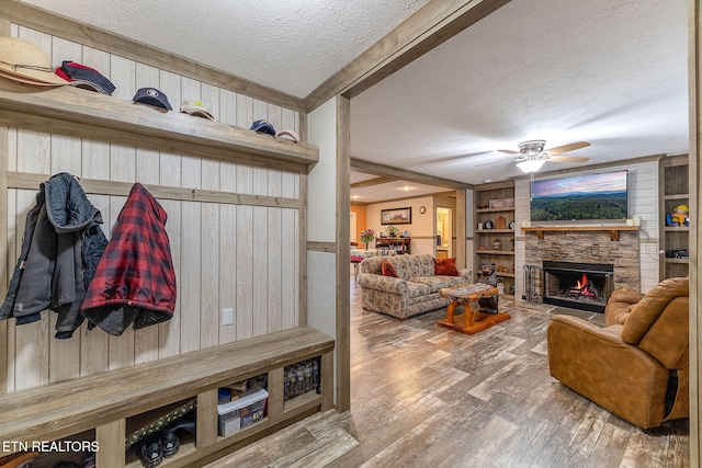 mudroom with a textured ceiling, ceiling fan, wooden walls, hardwood / wood-style flooring, and a stone fireplace