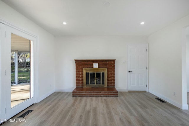 unfurnished living room featuring light hardwood / wood-style flooring and a brick fireplace