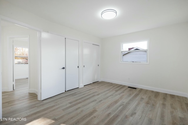 unfurnished bedroom with two closets, light wood-type flooring, and multiple windows