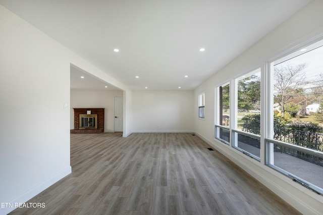 unfurnished living room with a brick fireplace and light wood-type flooring