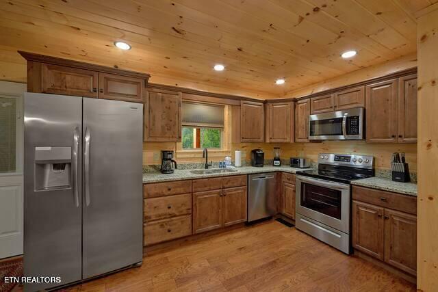 kitchen featuring light wood-type flooring, stainless steel appliances, light stone counters, and sink