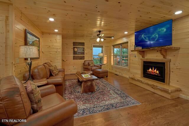 living room with wood-type flooring, ceiling fan, wooden ceiling, and wood walls