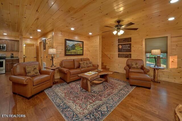 living room featuring hardwood / wood-style floors, ceiling fan, wood ceiling, and wooden walls