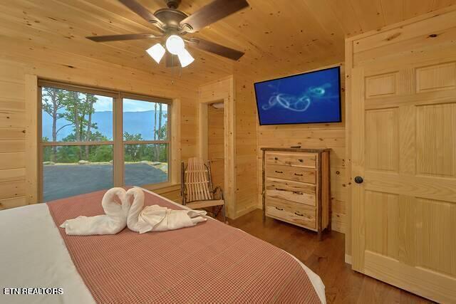 bedroom with lofted ceiling, ceiling fan, dark hardwood / wood-style floors, and wood walls