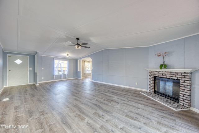 unfurnished living room with a brick fireplace, ceiling fan, vaulted ceiling, and light hardwood / wood-style flooring