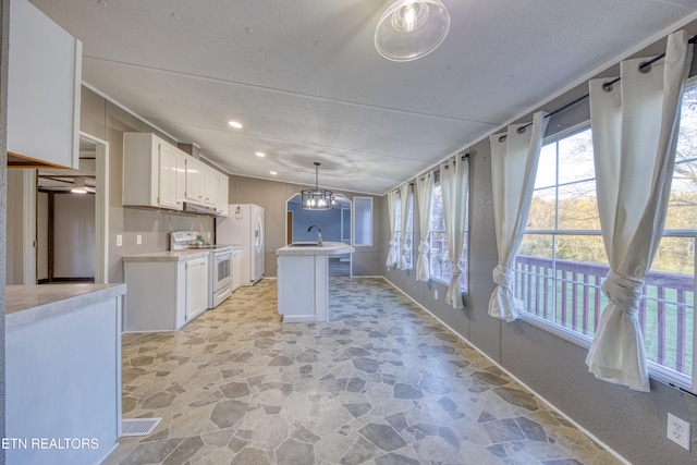 kitchen featuring white appliances, an inviting chandelier, white cabinets, sink, and an island with sink