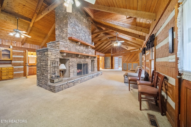 carpeted living room with wood walls, wooden ceiling, high vaulted ceiling, a stone fireplace, and beamed ceiling