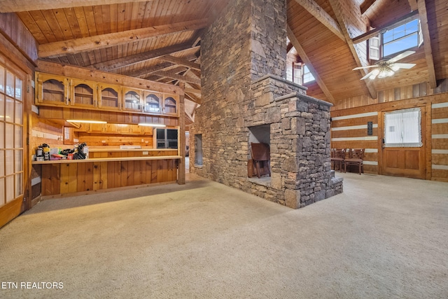 unfurnished living room featuring carpet flooring, high vaulted ceiling, plenty of natural light, and wood walls