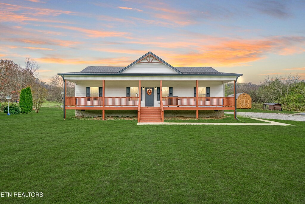 farmhouse with a lawn, a storage shed, and covered porch