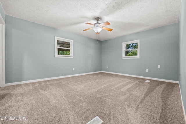 carpeted empty room with ceiling fan, plenty of natural light, and a textured ceiling