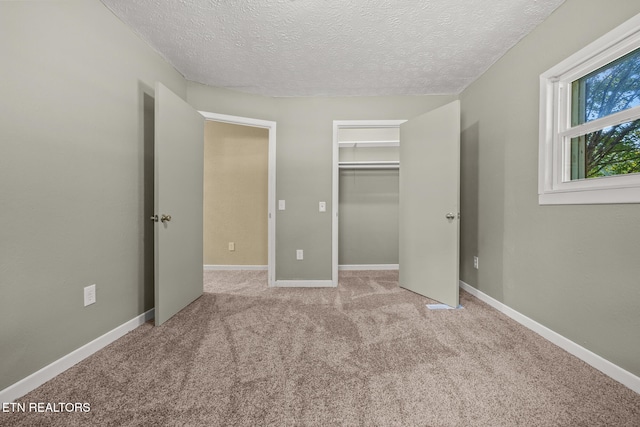 unfurnished bedroom with a textured ceiling, a walk in closet, light colored carpet, and a closet