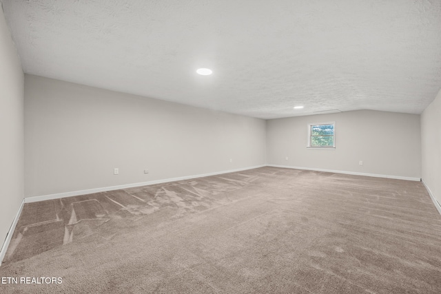 empty room featuring carpet, a textured ceiling, and vaulted ceiling