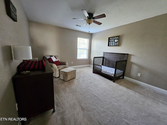 carpeted bedroom with ceiling fan and a crib