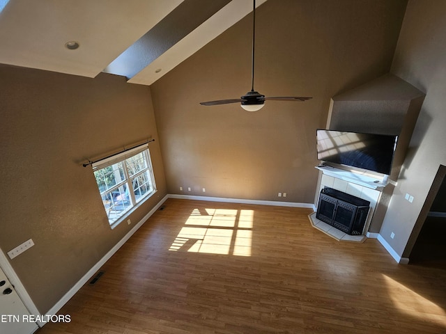 unfurnished living room with hardwood / wood-style flooring, high vaulted ceiling, ceiling fan, and a tiled fireplace