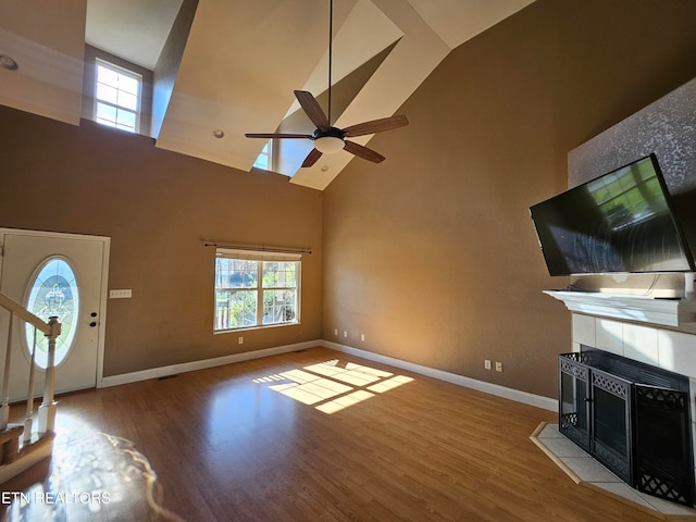 unfurnished living room featuring hardwood / wood-style flooring, ceiling fan, a tile fireplace, and high vaulted ceiling