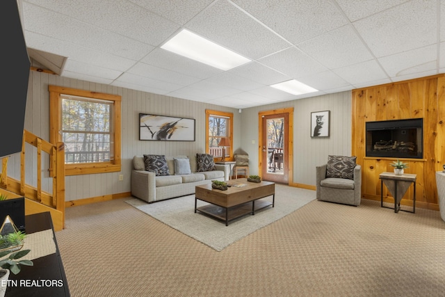 living room with a drop ceiling, carpet floors, and wooden walls