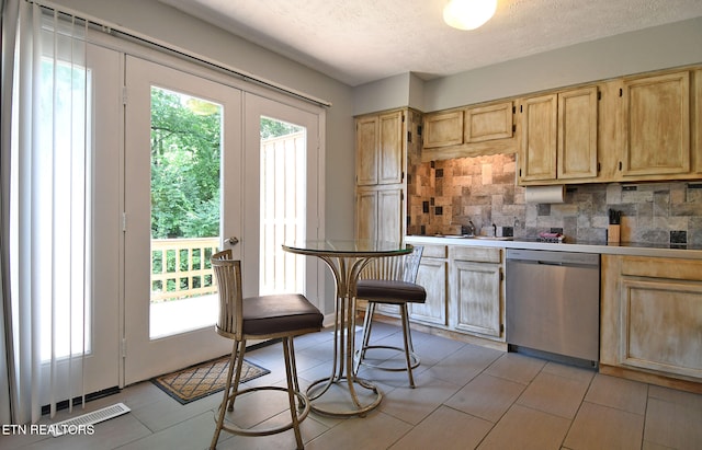 kitchen featuring stainless steel dishwasher, light brown cabinets, backsplash, and a textured ceiling