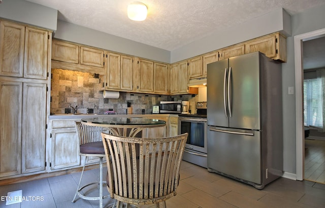 kitchen featuring light brown cabinetry, tasteful backsplash, custom range hood, a textured ceiling, and stainless steel appliances