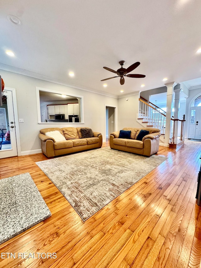 living room featuring decorative columns, light hardwood / wood-style flooring, ceiling fan, and ornamental molding