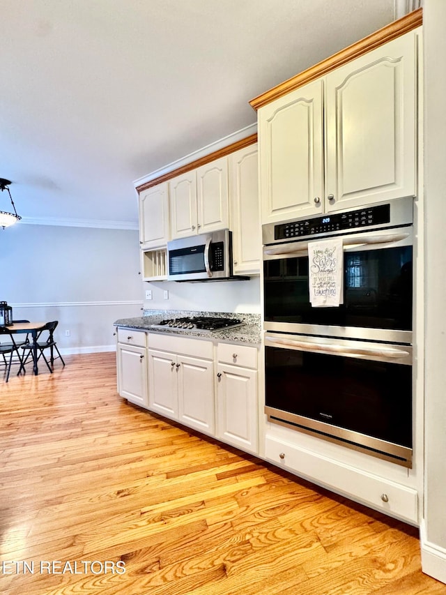 kitchen with appliances with stainless steel finishes, light wood-type flooring, and ornamental molding