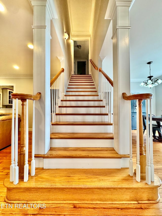 stairway with ornate columns, hardwood / wood-style floors, and ornamental molding