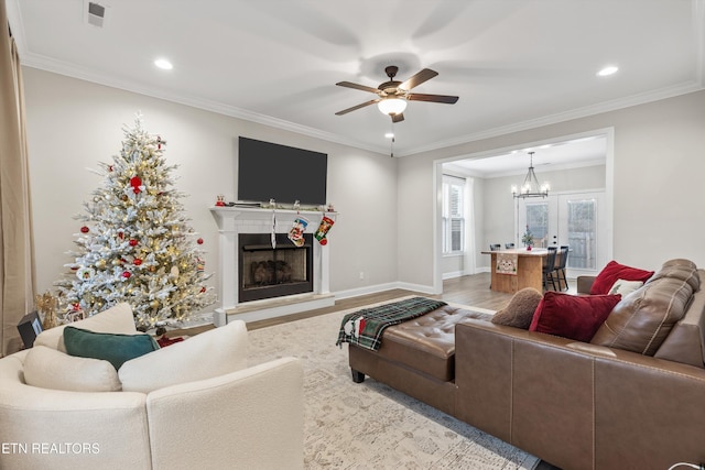 living room with ceiling fan with notable chandelier, light hardwood / wood-style floors, crown molding, and french doors