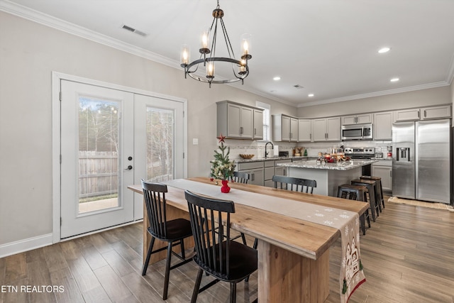 dining area with french doors, crown molding, dark wood-type flooring, sink, and an inviting chandelier