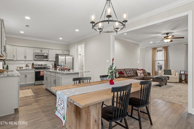 dining space featuring sink, dark wood-type flooring, ceiling fan with notable chandelier, and ornamental molding