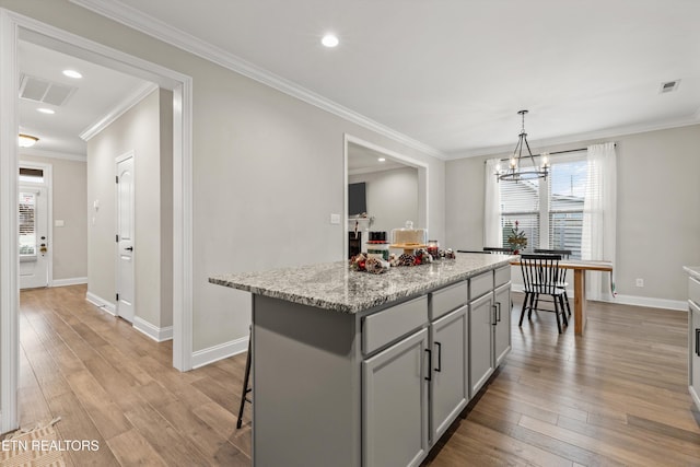 kitchen with gray cabinetry, light stone counters, crown molding, light hardwood / wood-style floors, and a kitchen island