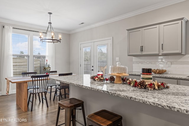 kitchen featuring light stone countertops, tasteful backsplash, light hardwood / wood-style floors, gray cabinets, and ornamental molding