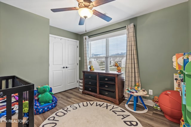 bedroom with hardwood / wood-style floors, ceiling fan, a closet, and a nursery area