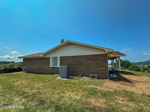 view of side of home featuring a yard, brick siding, and central AC