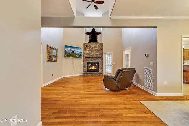 living room with ceiling fan, light wood-type flooring, a fireplace, a towering ceiling, and ornamental molding