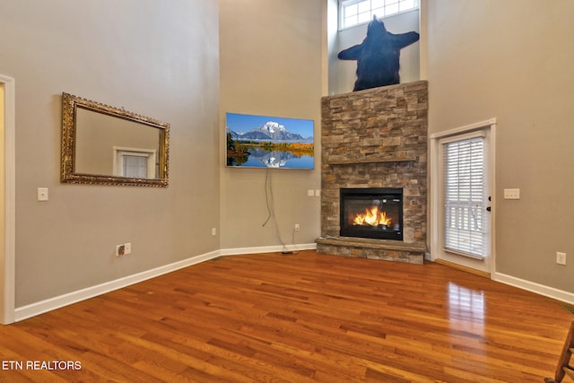 unfurnished living room with a high ceiling, hardwood / wood-style flooring, and a stone fireplace