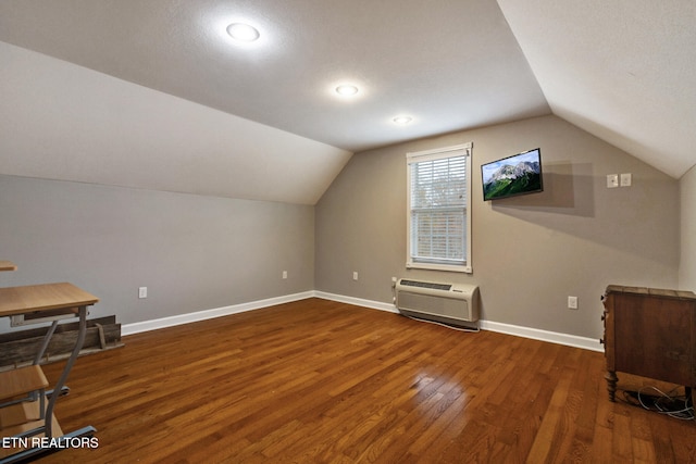 additional living space with a wall mounted air conditioner, dark hardwood / wood-style floors, lofted ceiling, and a textured ceiling