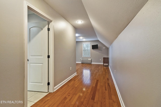 additional living space featuring a wall mounted air conditioner, light wood-type flooring, and lofted ceiling