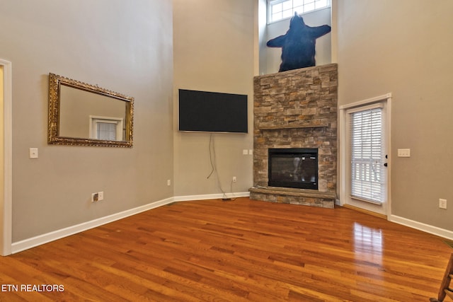 unfurnished living room with hardwood / wood-style flooring, a stone fireplace, and a high ceiling