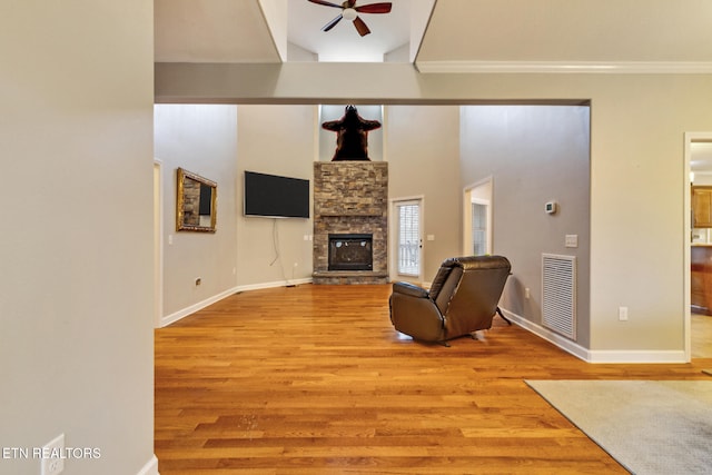 living room with ornamental molding, ceiling fan, light hardwood / wood-style flooring, a high ceiling, and a stone fireplace