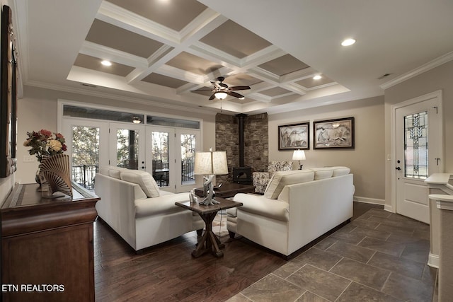 living room featuring ceiling fan, beam ceiling, coffered ceiling, ornamental molding, and a wood stove