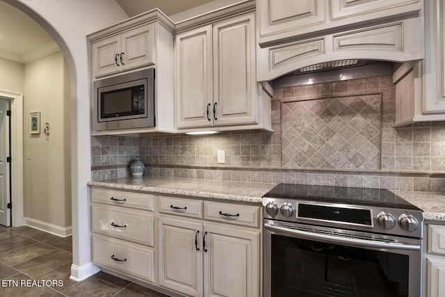 kitchen with appliances with stainless steel finishes, dark tile patterned flooring, custom exhaust hood, light stone counters, and cream cabinets