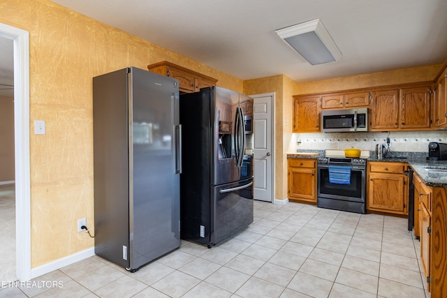 kitchen with light tile patterned floors, backsplash, appliances with stainless steel finishes, and dark stone counters